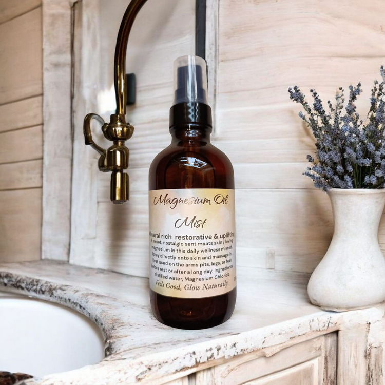 4 oz spray dark Boston bottle with a yellowish and white label that reads magnesium oil mist sitting on a counter side with some tan wooden plank walls with some brass faucet coming out the back side with a small plant with dried flowers and it next to it