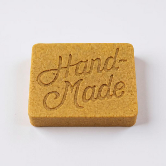 A soap bar orangish brown and tint with some speckles in it so breeds handmade on a white background with a light shadow