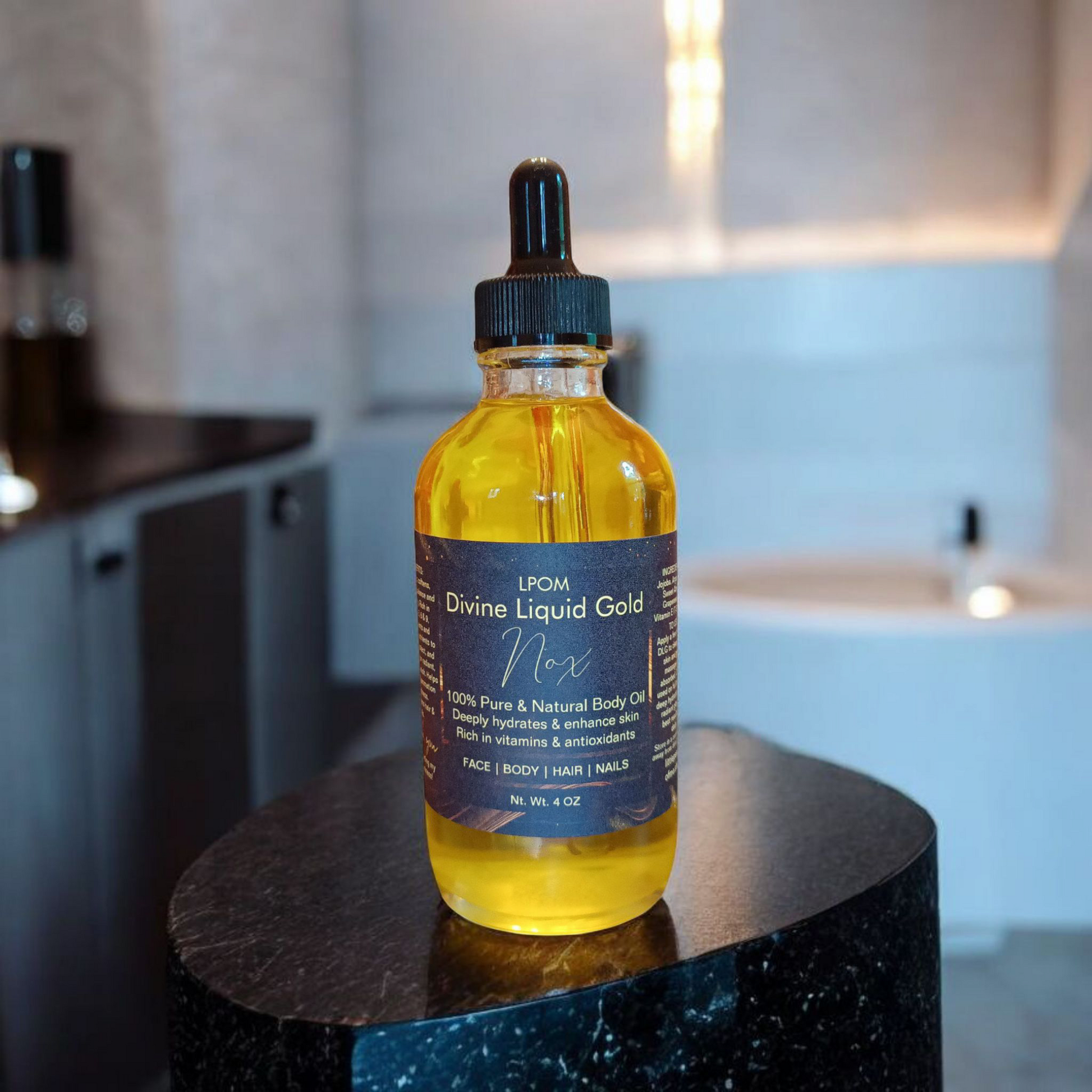 A 4 oz glass dropper bottle with a black label that reads Divine Liquid Gold body oil sent is called Nox sitting on a black sleek pedestal background of a white and black bathroom with lighting