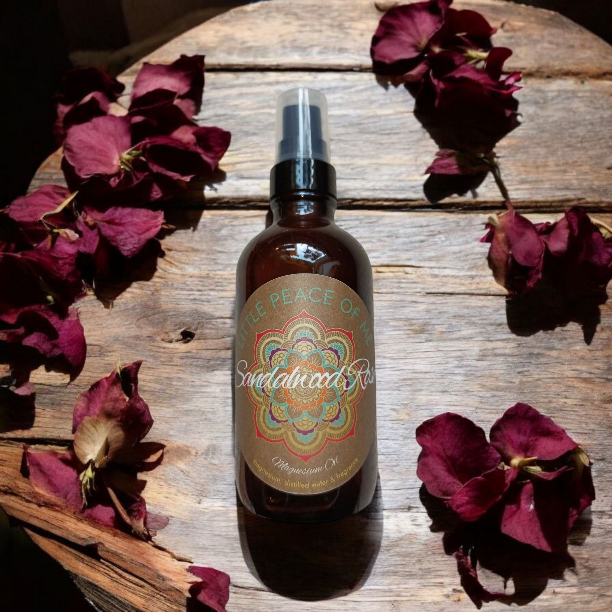4 oz glass Boston spray bottle with a tan label that reads little piece of me sandalwood Rose lighting coming through a window the bottle is displayed on a table with dried rose petals and pieces of sandalwood laid out around the bottle