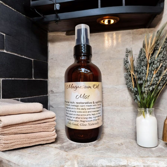4 oz Boston dark spray bottle with the yellowish and white label that reads magnesium oil mist sitting on a tan marble ledge with subway tile black sleek up the wall behind it a small light comes down over it sitting next to the bottle or some washcloths and on the other side is a small decoration holding dry flowers