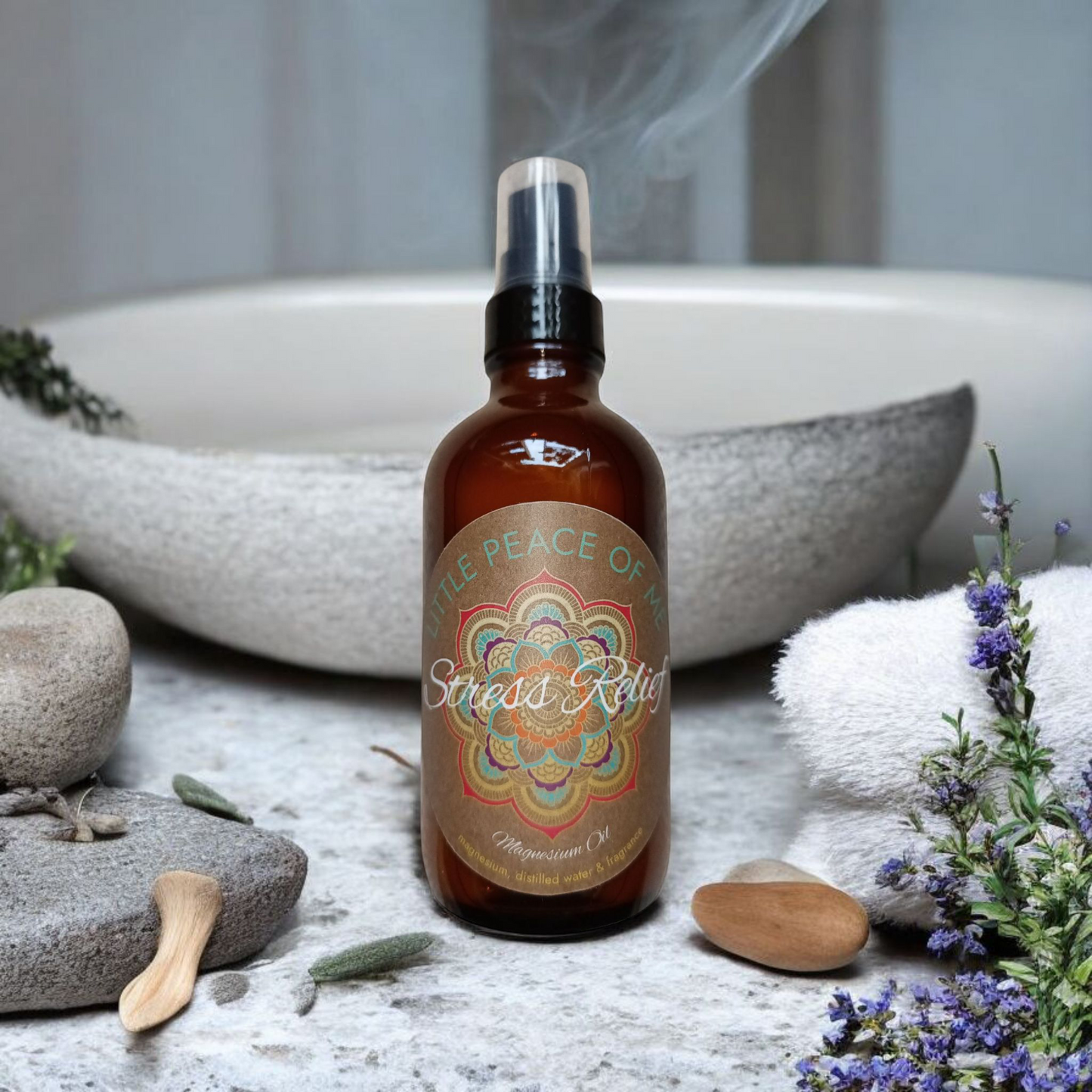 4 oz Boston dark spray bottle that reads Little piece of Me stress relief centered in the middle surrounded by flat slate rocks some dried lavender lays alongside in a Zen bathroom vibe with a towel and a sink behind it in a white wall that runs up the back