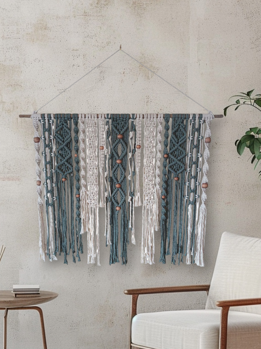Tealish and white macrame knots wall hanging on a wall next to setting small table and chair and a plant