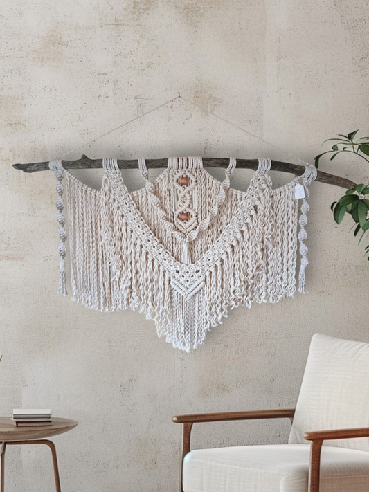 Macrame wall hanging and driftwood White Fringe on a wall next to a table and chairs and a plant and a small setting